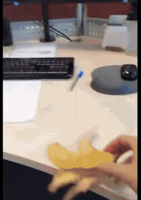 a person holding a banana on a desk next to a keyboard