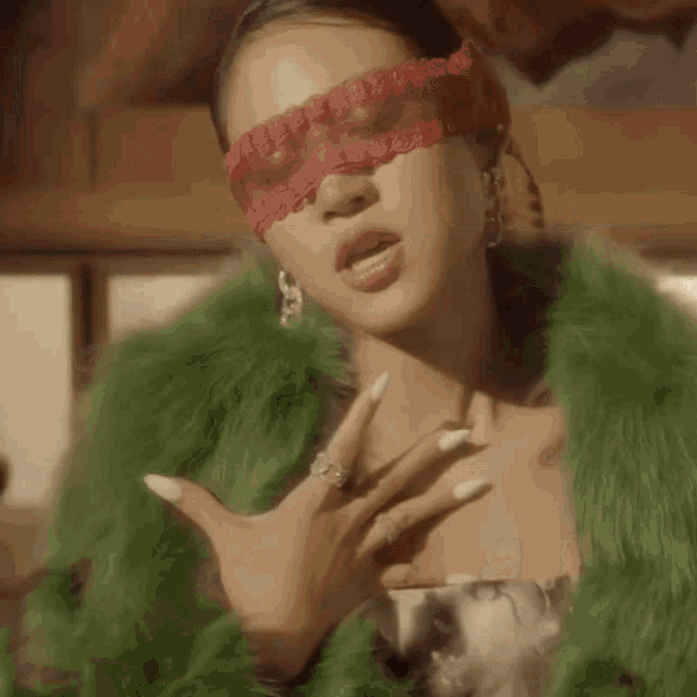 a woman in a green fur coat is wearing a red lace blindfold