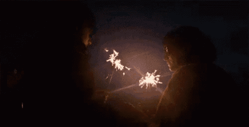 a man and a woman are holding sparklers in their hands in the dark .