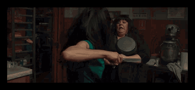 a woman holding a frying pan and a knife in a kitchen