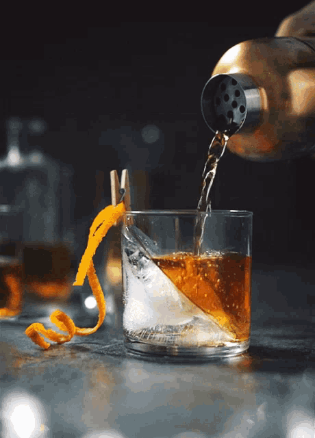 a drink is being poured into a glass with ice and an orange peel