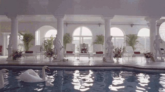 a swan is swimming in a swimming pool with statues around it