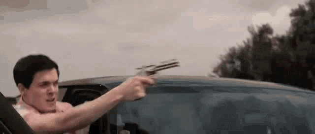 a man is driving a car and pointing a gun out the window .