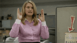 a woman in a pink shirt is making a gesture with her hands in front of a sign that says please .