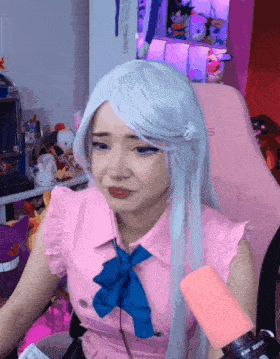 a woman wearing a wig and a pink shirt is sitting in a pink chair with the letter s on it