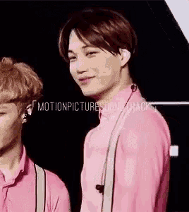 a man in a pink shirt and suspenders is smiling while standing next to another man .
