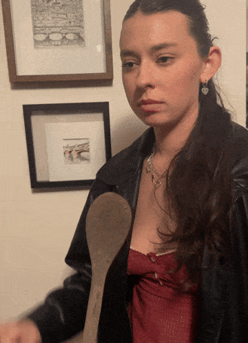 a woman in a leather jacket holds a wooden spoon in her hand