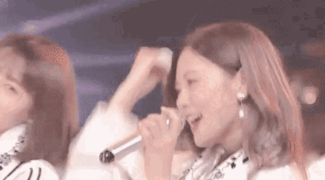 a woman is singing into a microphone while standing next to another woman .