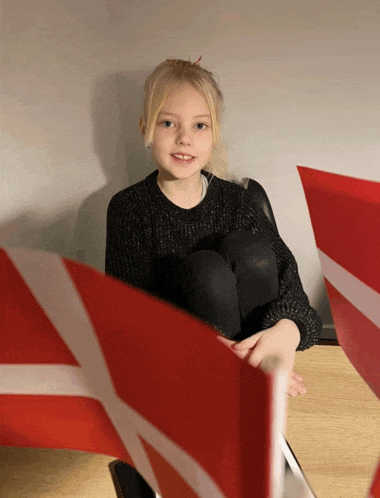 a little girl is sitting on a table with a red and white flag in front of her