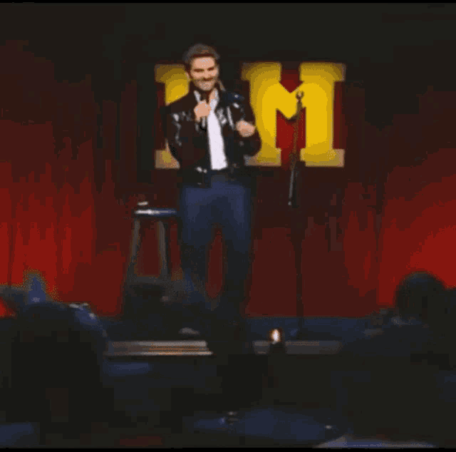 a man in a black jacket is standing in front of a microphone on a stage .