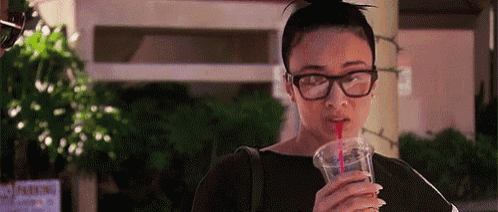 a woman wearing glasses is drinking a drink from a plastic cup with a straw .