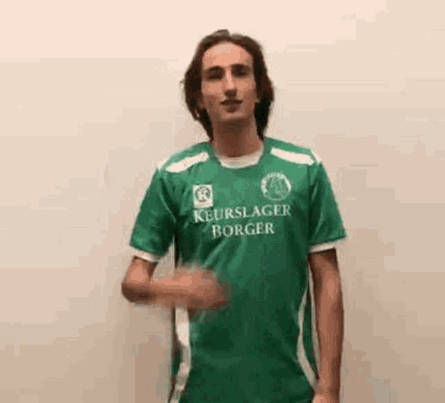 a young man in a green soccer jersey is making a funny face .