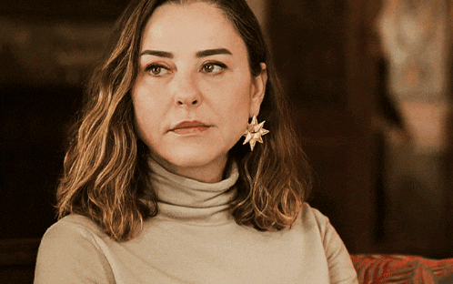 a woman wearing a turtleneck and star shaped earrings looks at the camera