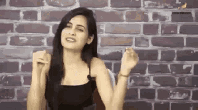 a woman in a black tank top is standing in front of a brick wall .
