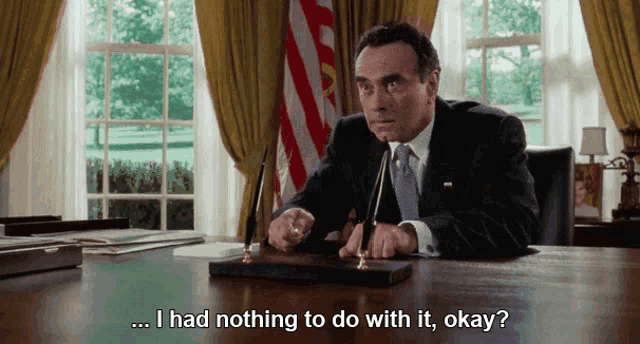 a man in a suit sits at a desk with the words " i had nothing to do with it okay " below him
