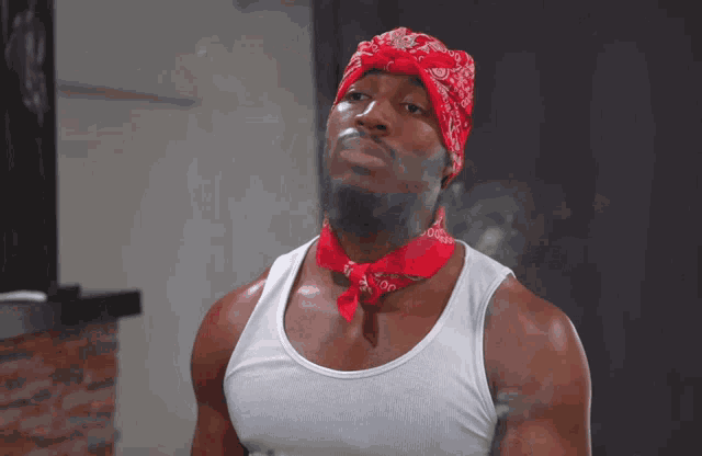 a man wearing a red bandana and a white tank top smoking a cigarette