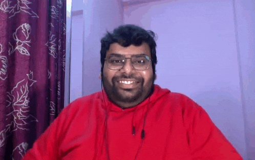 a man wearing glasses and a red hoodie is smiling while looking at the camera .