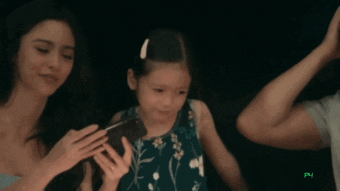 a little girl is looking at a cell phone while a man and woman look on with the letters pn visible in the corner
