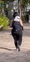 a woman with a backpack is walking down a sidewalk .