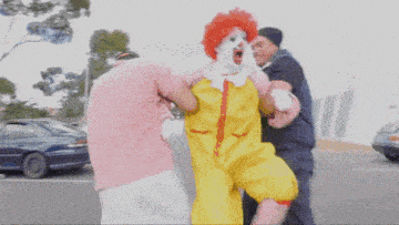 a man in a mcdonalds clown costume is being held by two men