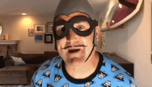 a man wearing a superhero mask and a hat is standing in a living room
