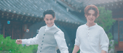 two men are holding hands in front of a building and smiling