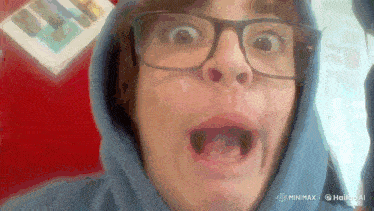 a man wearing glasses and a blue hoodie makes a funny face
