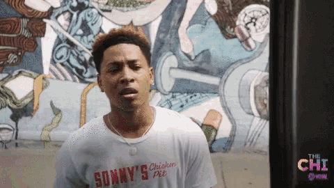 a man wearing a sonny 's chicken pit shirt stands in front of a wall
