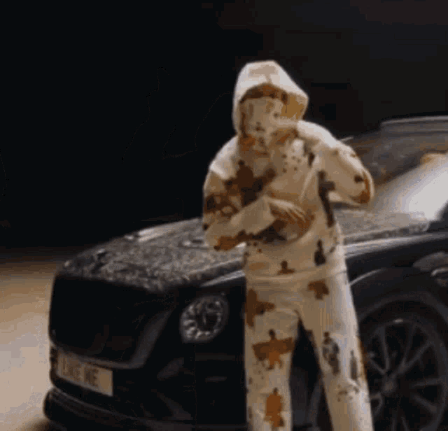 a man in a hoodie is standing in front of a bentley car