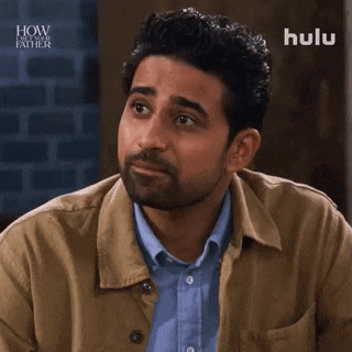 a man with a beard is wearing a tan jacket and a blue shirt and making a funny face .