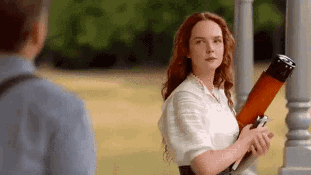 a woman with red hair is holding a large object in her hand while standing next to a man .