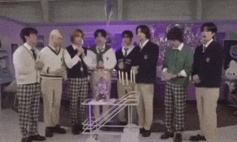 a group of young men in school uniforms are standing around a table with candles on it .