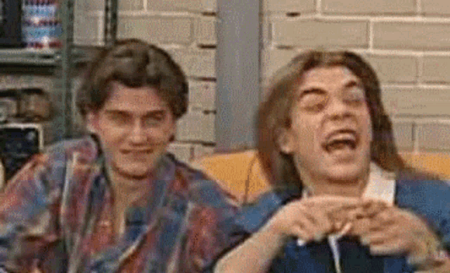 two young men are sitting next to each other on a couch laughing .