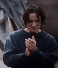 a man in a blue sweater is clapping his hands together in a close up .