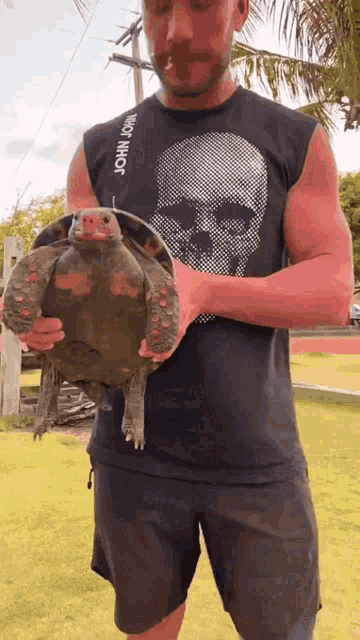 a man holding a turtle wearing a black shirt that says john john