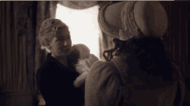 a woman in a hat holds a baby in her arms while another woman looks on