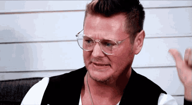 a man wearing glasses and a black vest is making a face