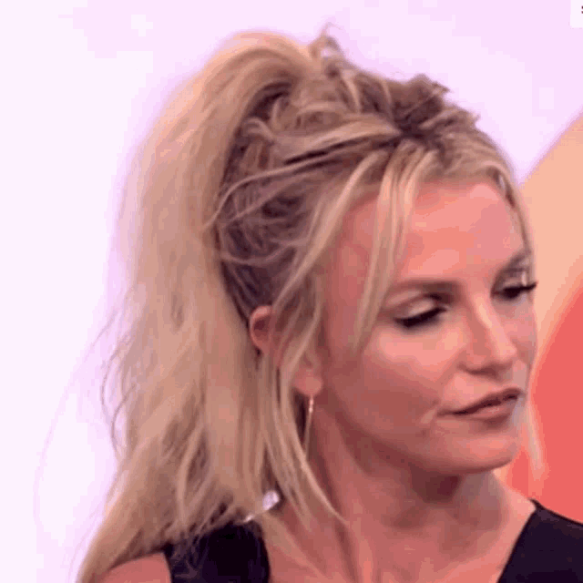 a close up of a woman 's face with blonde hair in a ponytail and earrings .