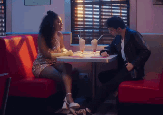 a man and a woman are sitting at a diner table with milkshakes