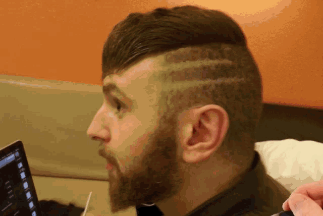 a man with a shaved design on his head looks at a laptop screen