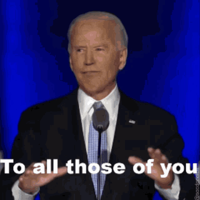 a man in a suit and tie is speaking into a microphone with the words to all those of you above him