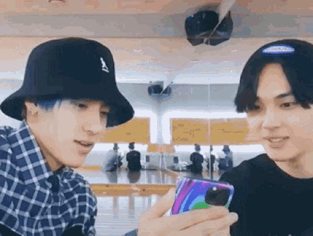 two young men wearing hats are looking at a cell phone together .