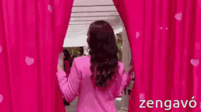 a woman in a pink jacket is standing behind a pink curtain ..