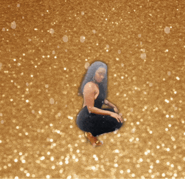 a woman in a black jumpsuit is squatting down in front of a gold background