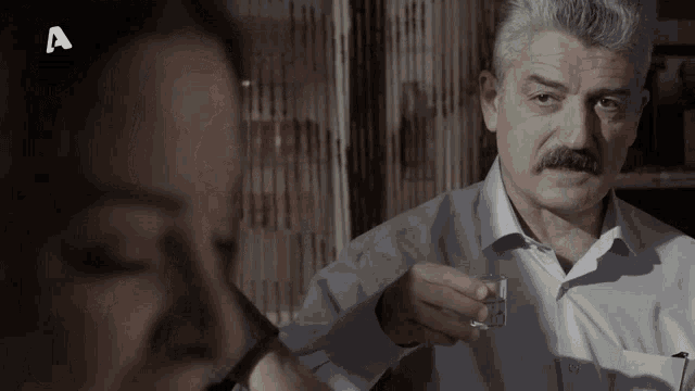 a man with a mustache is holding a glass in front of a woman with the letter a on the bottom
