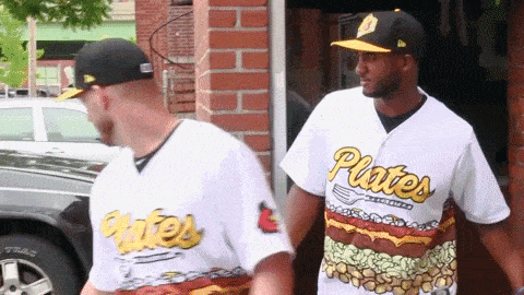 two baseball players wearing plates jerseys are walking down the street