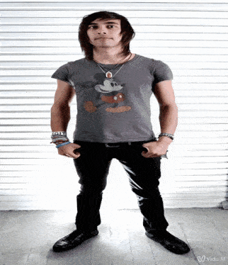 a young man wearing a mickey mouse t-shirt is standing with his hands in his pockets
