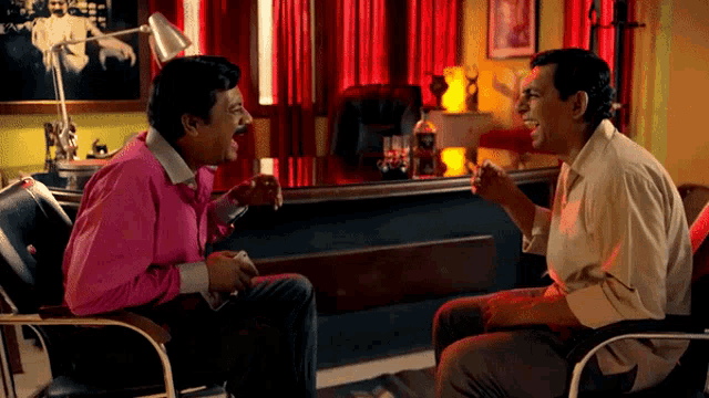 a man in a pink shirt laughs while sitting next to another man
