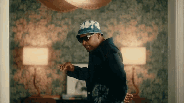 a man wearing a bucket hat and sunglasses is dancing in a room
