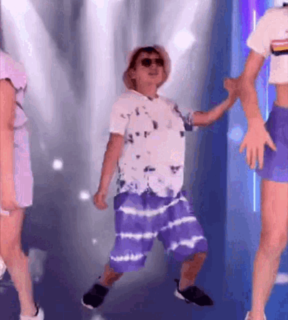 a boy in a hat and tie dye shorts is dancing in a room with two women .